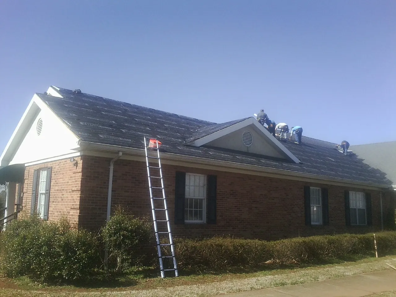 Crew tearing shingles off a brick ranch roof with a ladder set — Metal Roof Repair work by our crew in Piru