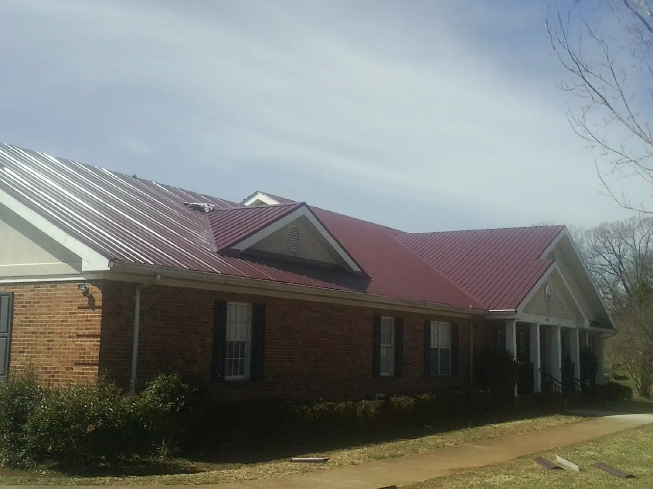 Red metal roof with gabled entries on a long brick building, from a Hail Damage Roof Repair job in Piru