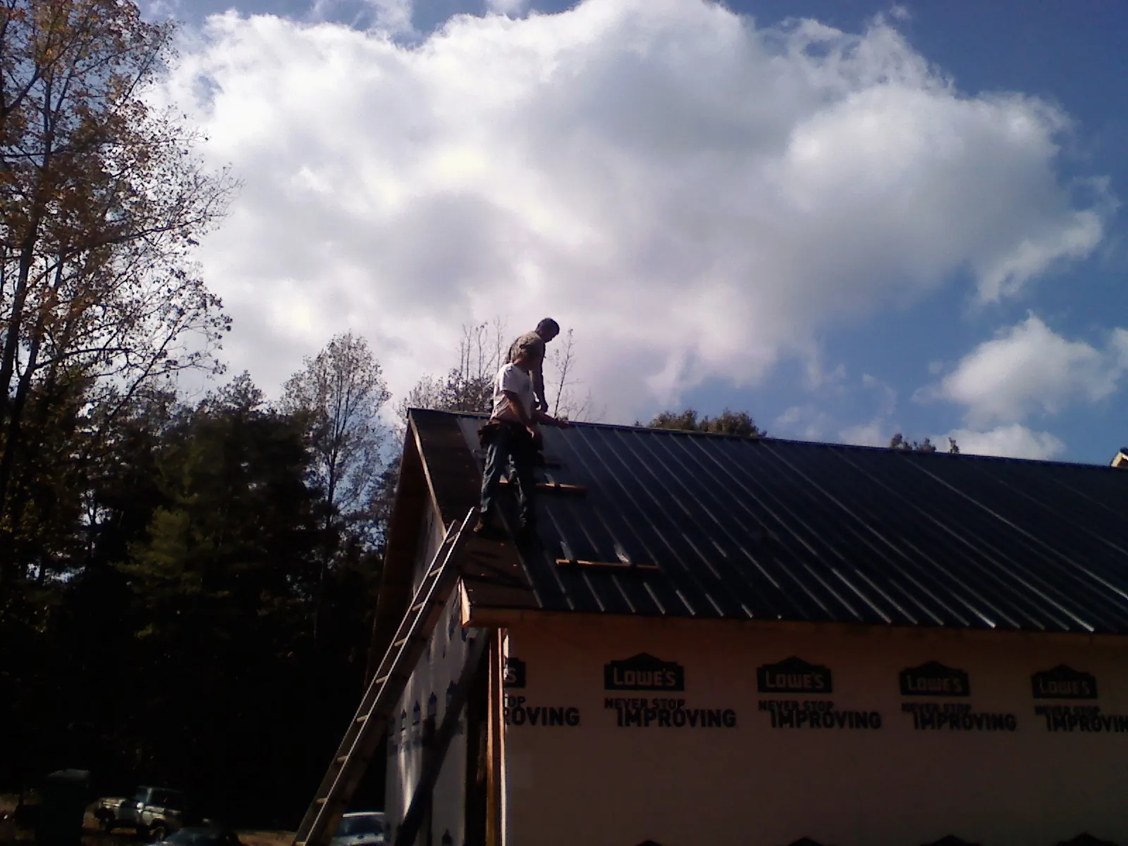 Roofer fastening dark metal panels high against a cloudy sky, from a Roof Inspection job in Piru